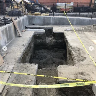 A trench dug out inside a concrete structure, marked off with caution tape