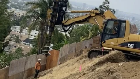 A drill rig working on a steep hillside lot